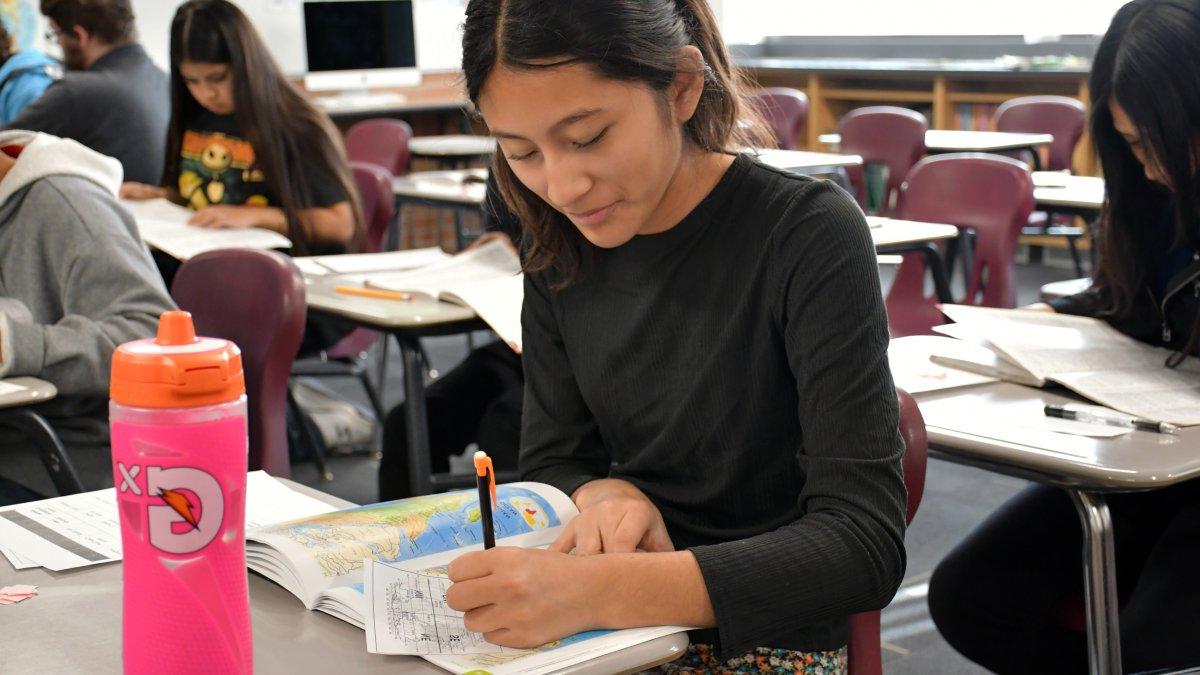 student writing with a map book open on her desk